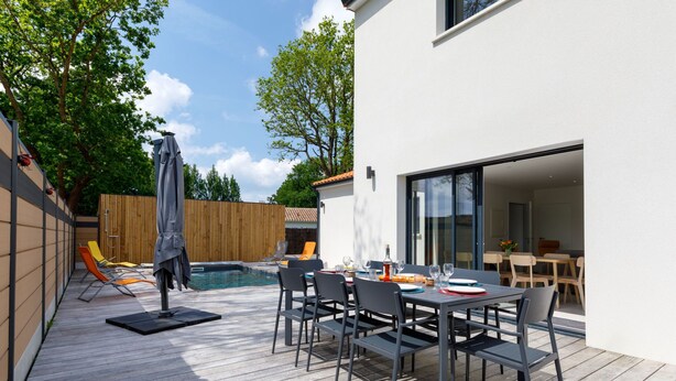 A modern outdoor patio with a pool, dining area, and sliding glass doors leading to a living space. - Le Pré Tarin by Interhome (La Bernerie-en Retz)