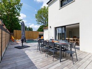 A modern outdoor patio with a pool, dining area, and sliding glass doors leading to a living space.