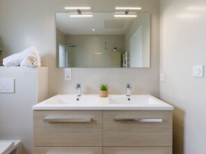 A modern bathroom with two sinks, a large mirror, and a potted plant.