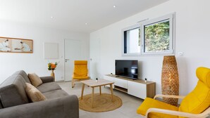 A modern living room with a grey sofa, a yellow armchair, a TV, and a window with a view of greenery. - Le Pré Tarin by Interhome (La Bernerie-en Retz)