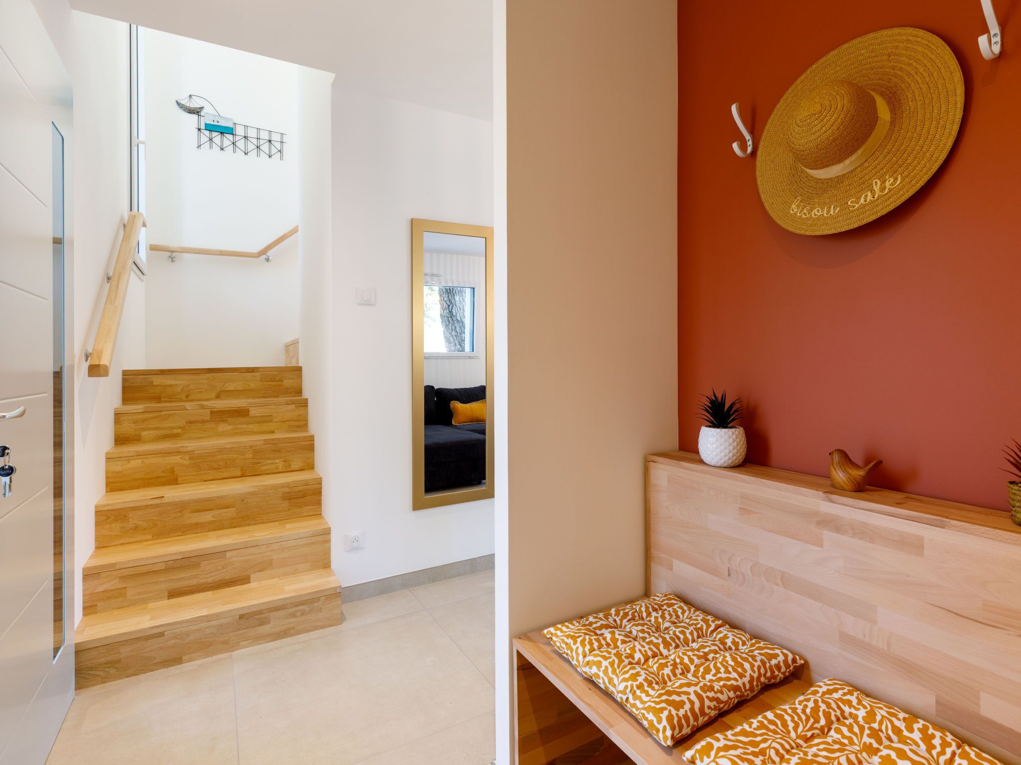 Un intérieur moderne avec un escalier en bois, un miroir, un canapé agrémenté de coussins à motifs et un chapeau accroché au mur.