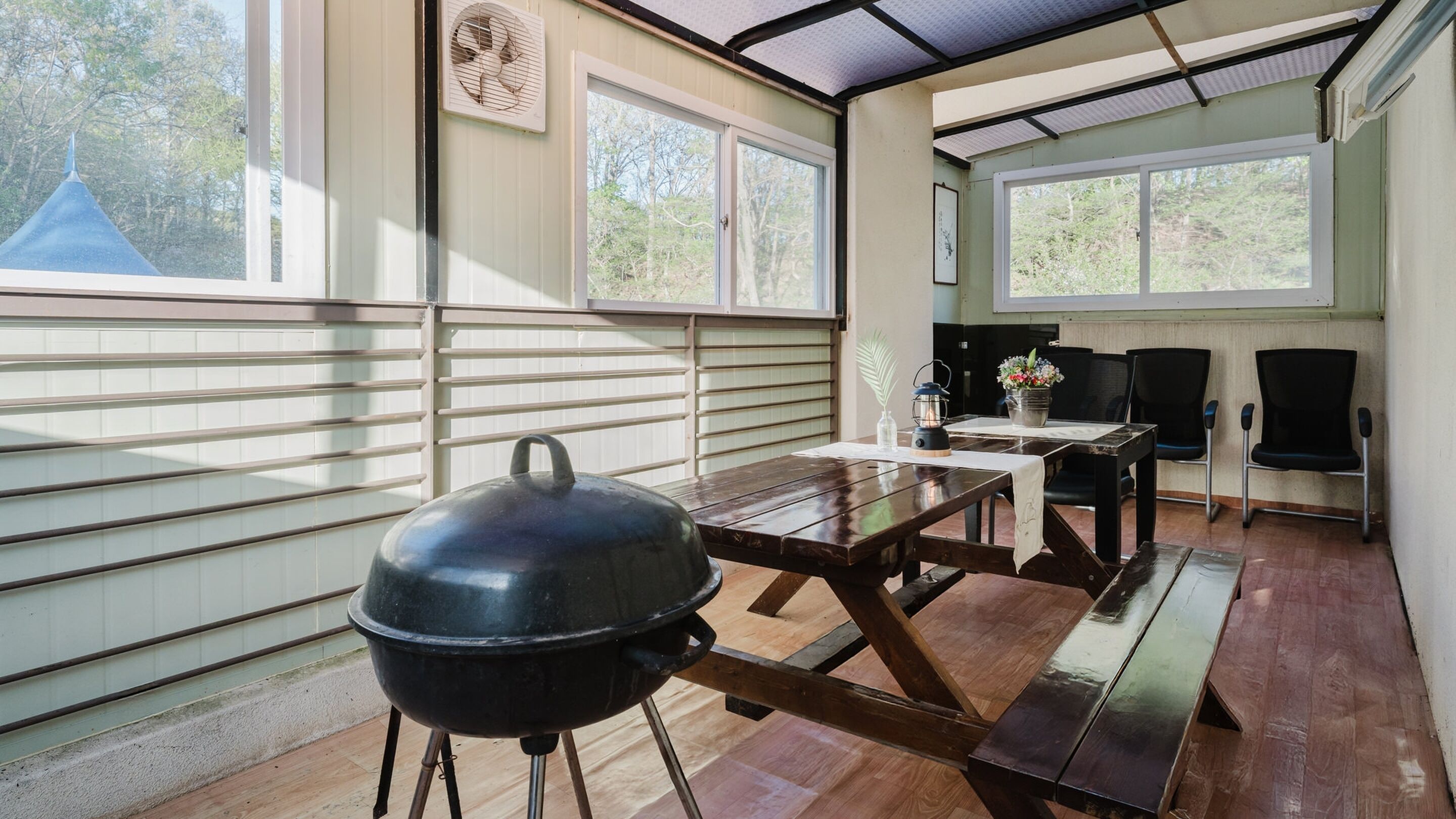 A dining area with a wooden table, chairs, a grill, and large windows with blinds.