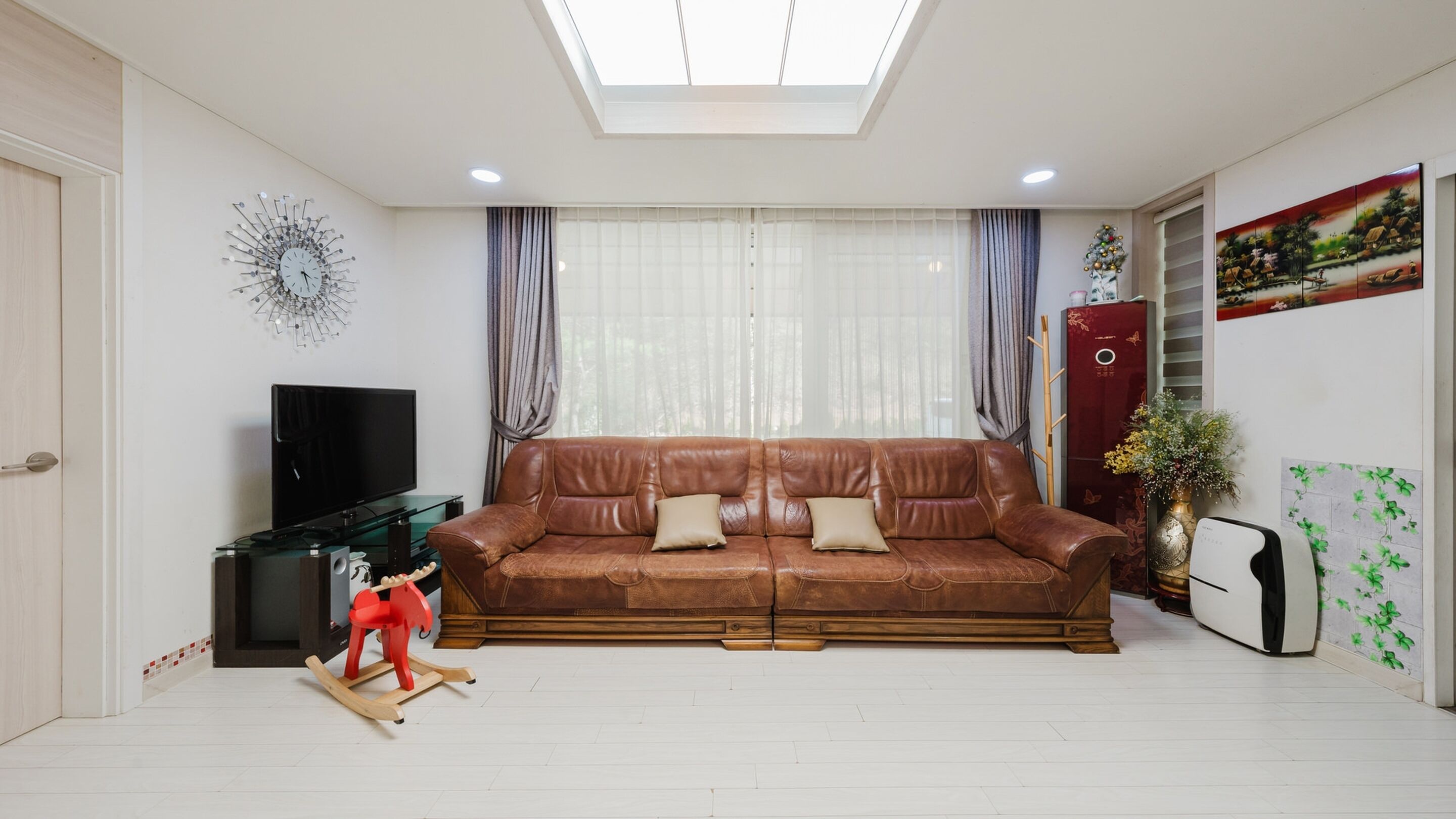 A living room with a brown leather sofa, a television, a red rocking horse, and a decorative wall piece.