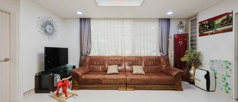 A living room with a brown leather sofa, a television, a red rocking horse, and a decorative wall piece.