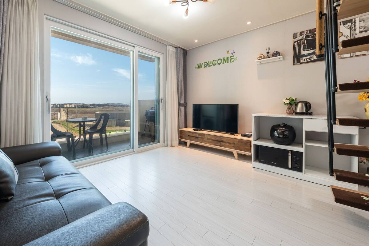 Una sala de estar moderna con un sofá de cuero, un televisor de pantalla plana y una puerta corrediza de vidrio que da a un patio al aire libre.
