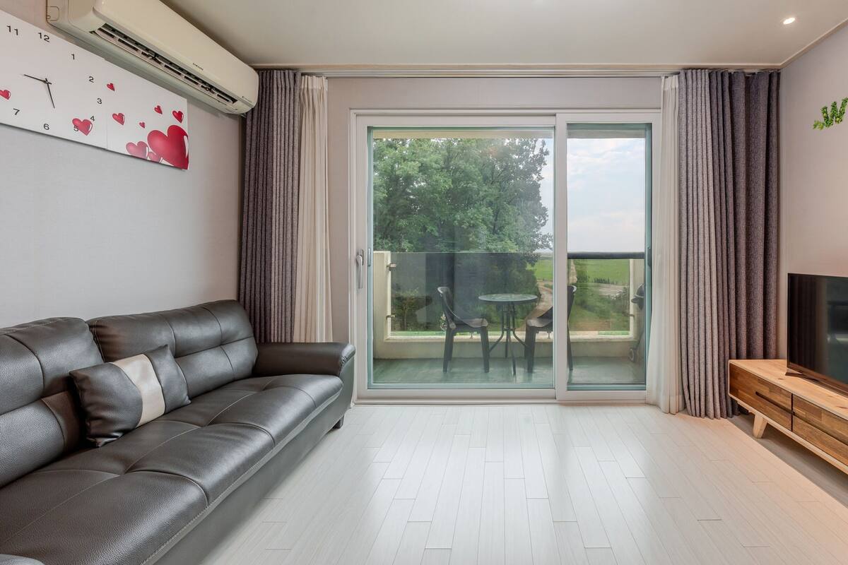 Una sala de estar moderna con un sofá de cuero, un televisor de pantalla plana y un gran ventanal corredero que da a un espacio exterior.