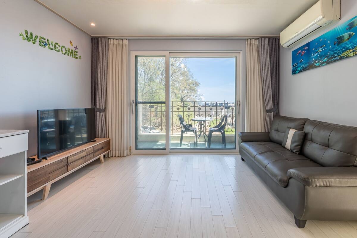 Una sala de estar moderna con televisor de pantalla plana, un sofá de cuero y un balcón con vistas.
