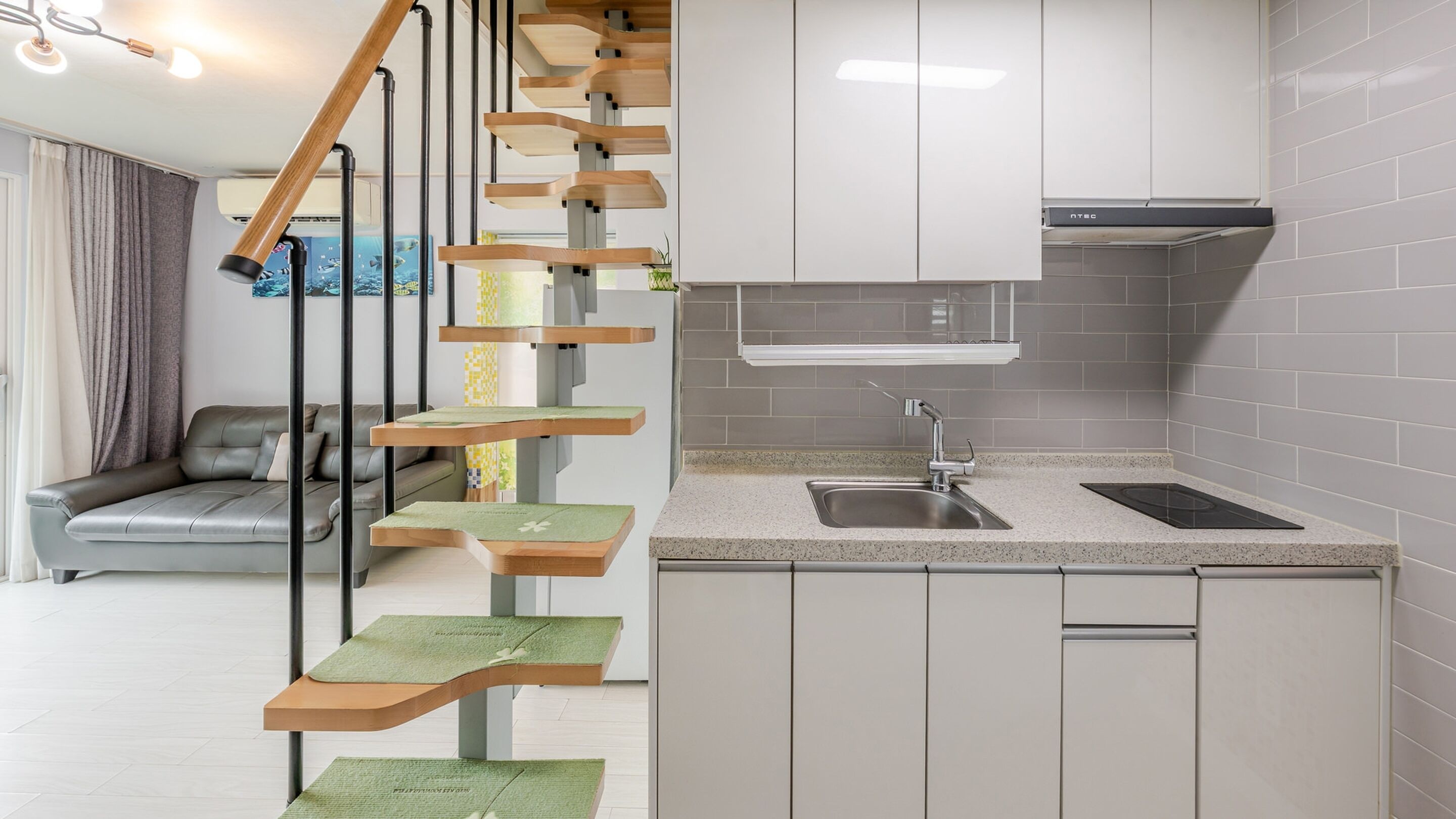 Een moderne keuken met een ingebouwde kookplaat, een spoelbak en een houten trap met groene matten.