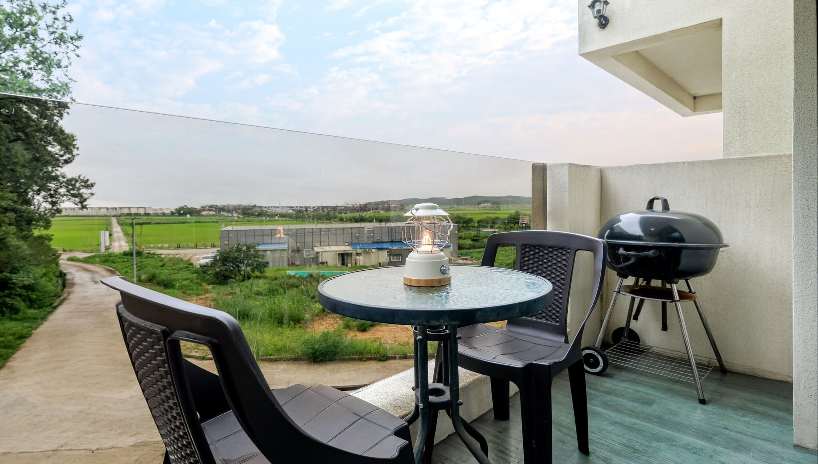 A balcony with a round table, two chairs, a portable grill, and a lantern.