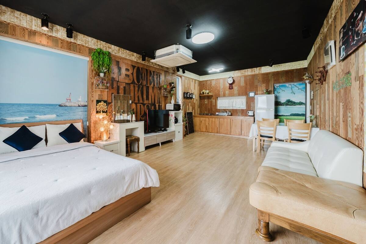 Un dormitorio con una cama grande, un sofá pequeño, un televisor y una zona de cocina.
