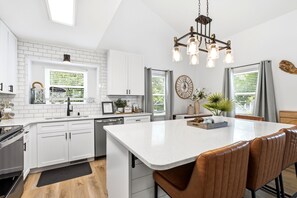 A modern kitchen with white cabinetry, a central island, and a dining area with leather chairs.