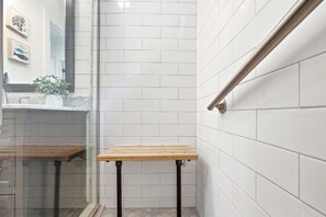 A bathroom with white tiled walls, a wooden bench, and a glass shower enclosure.