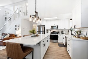 A modern kitchen with white cabinetry, stainless steel appliances, a central island, and a staircase leading to an upper level.