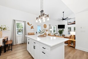 A modern kitchen with a central island, wooden flooring, and a ceiling fan.