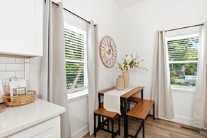 A kitchen with a wooden table, chairs, a clock, and a basket on the counter.