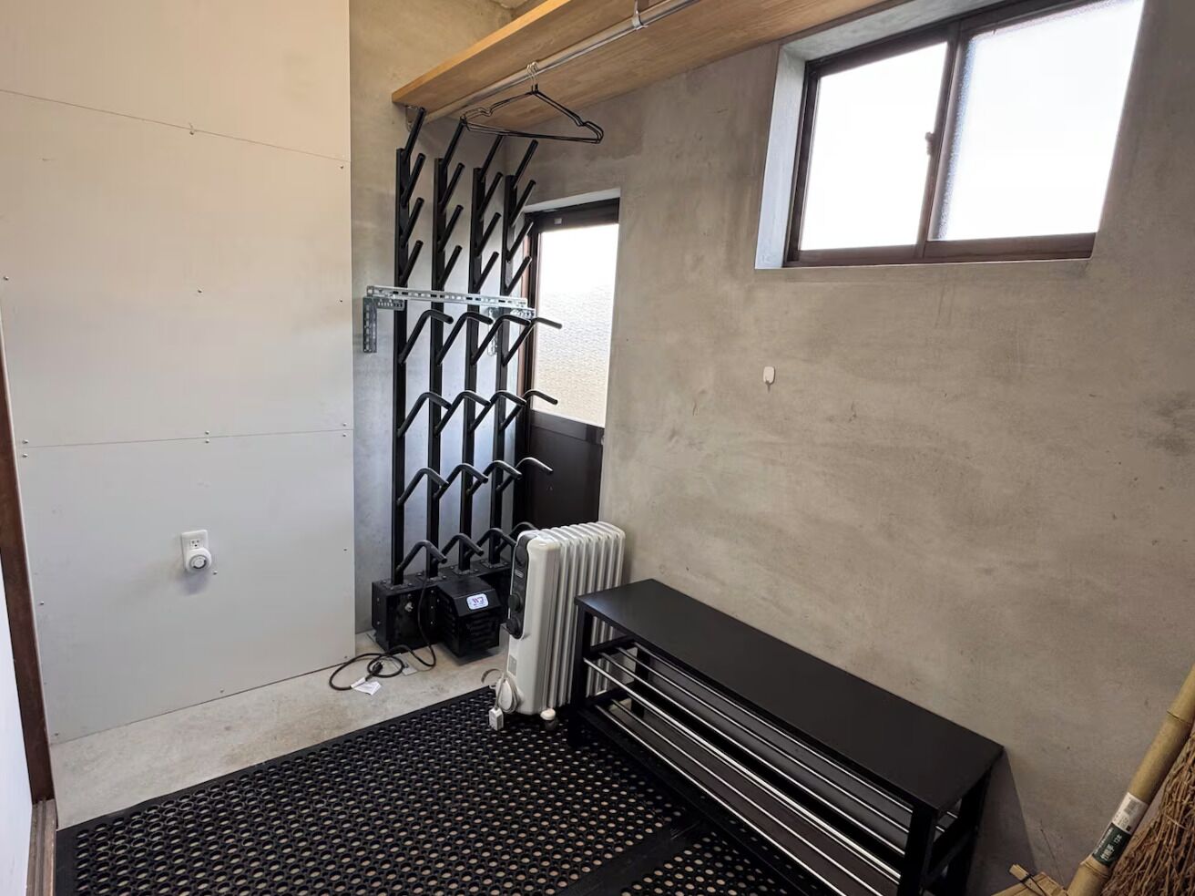 A small, industrial-style room with a radiator, a black bench, and a metal rack with hooks.