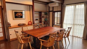 Una sala da pranzo tradizionale in stile giapponese, con un tavolo e sedie in legno, una mensola con oggetti decorativi e una finestra con tende.