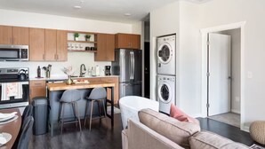 Una cocina moderna con una isla central, taburetes de bar, un refrigerador y una lavadora.