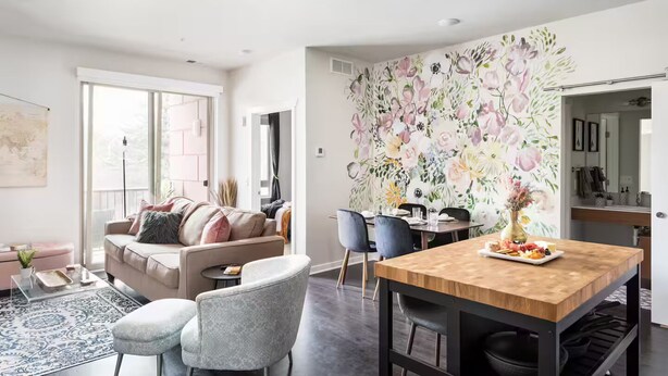 Una sala de estar moderna con un sofá, sillas, una mesa de comedor y un gran mural floral.