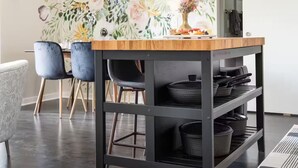 Un área de cocina con encimera de madera, estanterías negras y papel tapiz con motivos florales.
