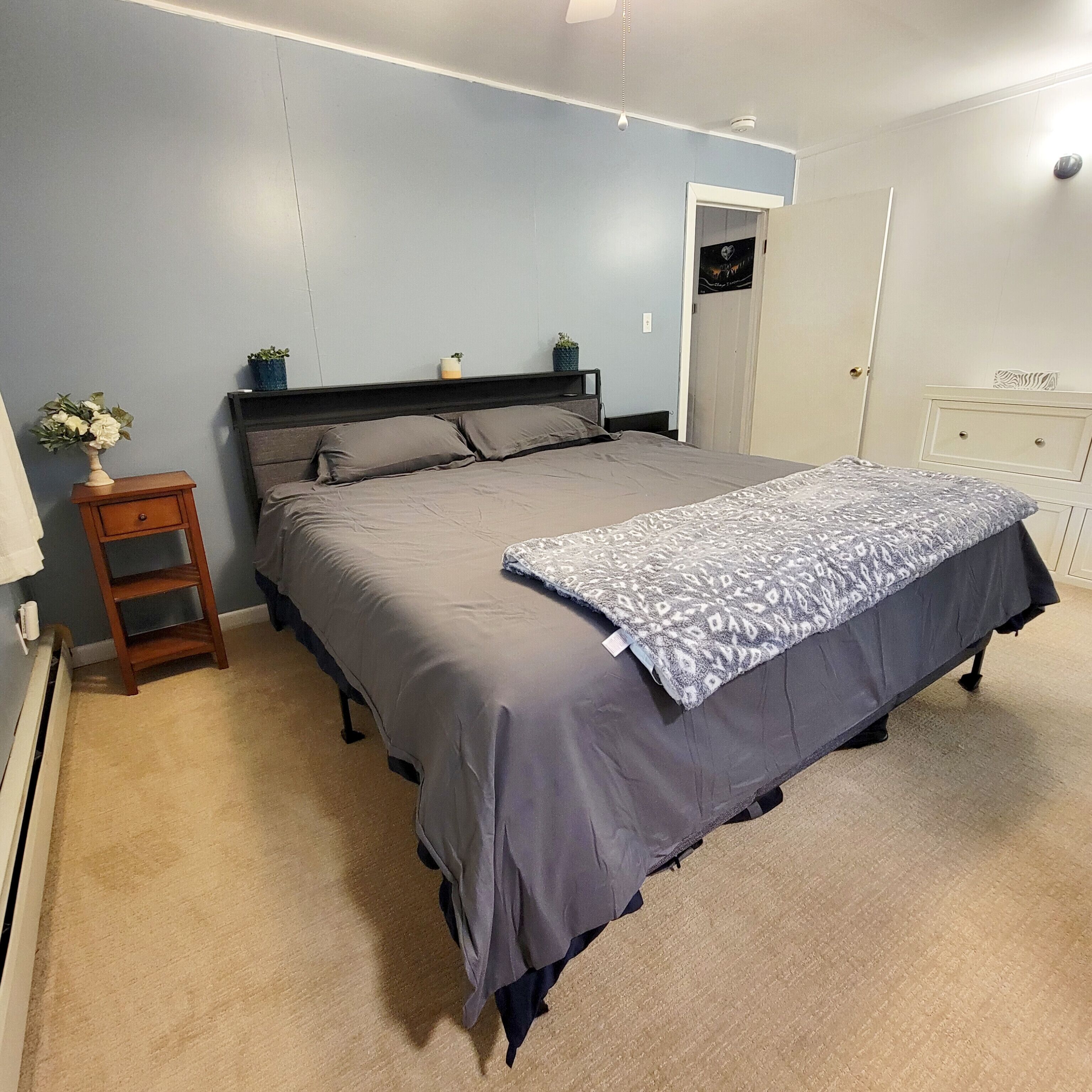 Un dormitorio con cama, mesita de noche, cómoda y puerta.