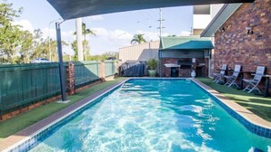 A swimming pool with a brick wall and a covered area with lounge chairs. - Arabella Motor Inn (Tweed Heads South)