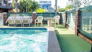 A swimming pool with a tiled edge, surrounded by a brick wall and a green artificial turf area. There are white plastic chairs and a table. - Arabella Motor Inn (Tweed Heads South)