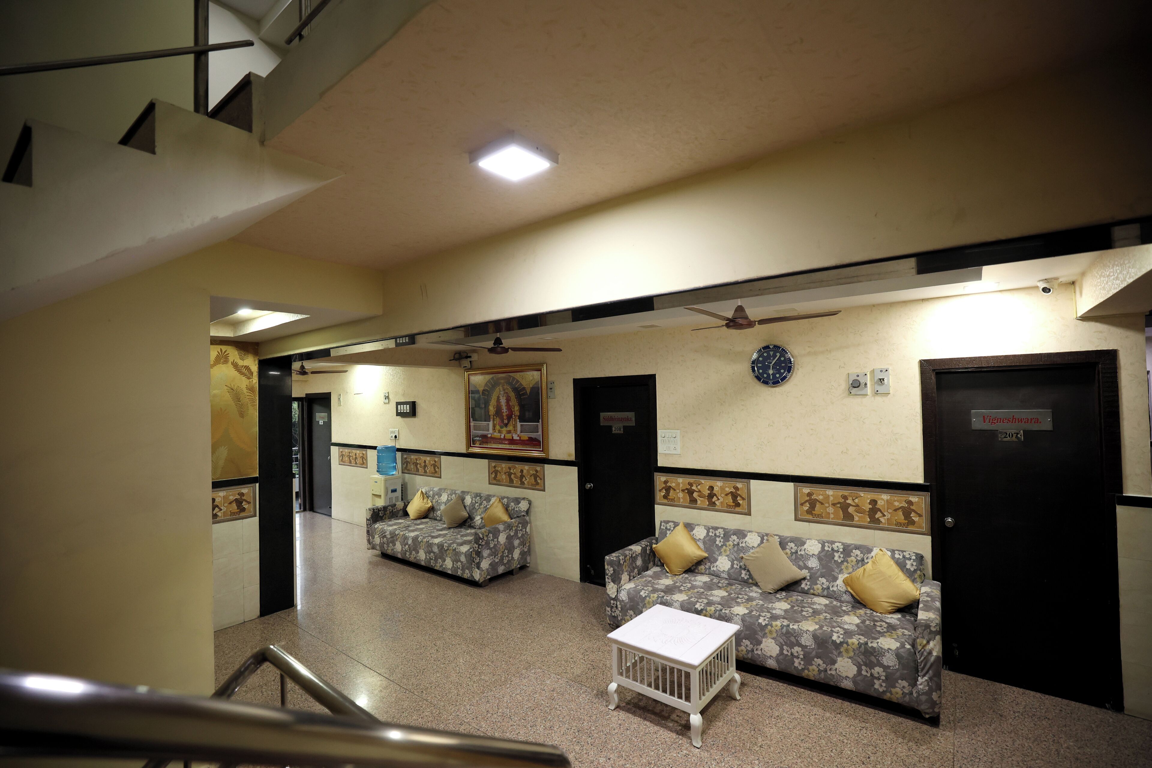 A lobby with two sofas, a small table, ceiling fans, and a clock on the wall.