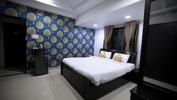 A bedroom with a bed, a dresser, a small table, and a refrigerator.