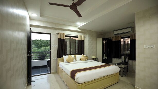 A hotel room with a bed, a ceiling fan, a window with curtains, and a balcony. - Hotel Park Gardenia (Nagpur)