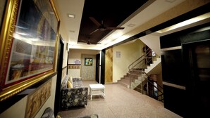 A hotel lobby with a sofa, a small table, a ceiling fan, and a staircase leading to an upper floor. - Hotel Park Gardenia (Nagpur)