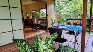 A room with a wooden floor, a bed with a blue bedspread, a desk with a chair, and a window.