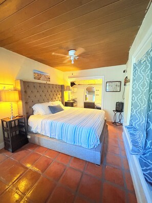 Une chambre à coucher avec un lit, des tables de chevet, un ventilateur de plafond et un sol carrelé.