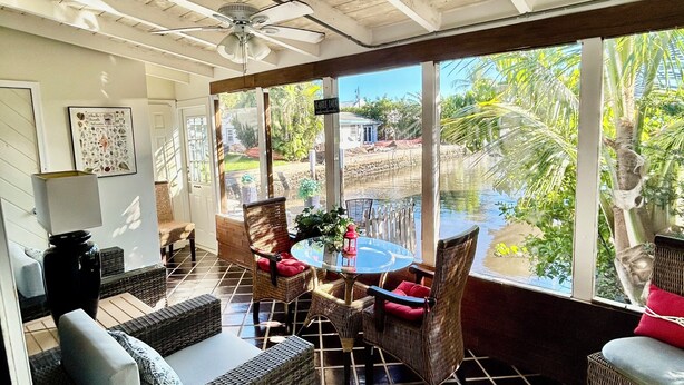 Un patio couvert aménagé avec des meubles en osier, une table ronde et un ventilateur de plafond.