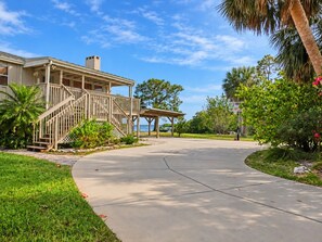 A residential property with a covered porch, a staircase, and a paved driveway leading to a gated entrance.