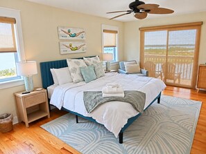 A bedroom with a bed, a nightstand, a lamp, a ceiling fan, and a view of the outdoors.