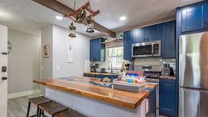 Een moderne keuken met blauwe kastjes, een houten kookeiland, roestvrijstalen apparatuur en een hangende lamp.