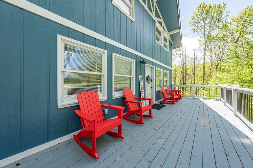 Un edificio azul con detalles blancos y una terraza de madera con sillas Adirondack rojas.