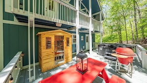 Een houten blokhut met een veranda, een barbecue en een lantaarn.