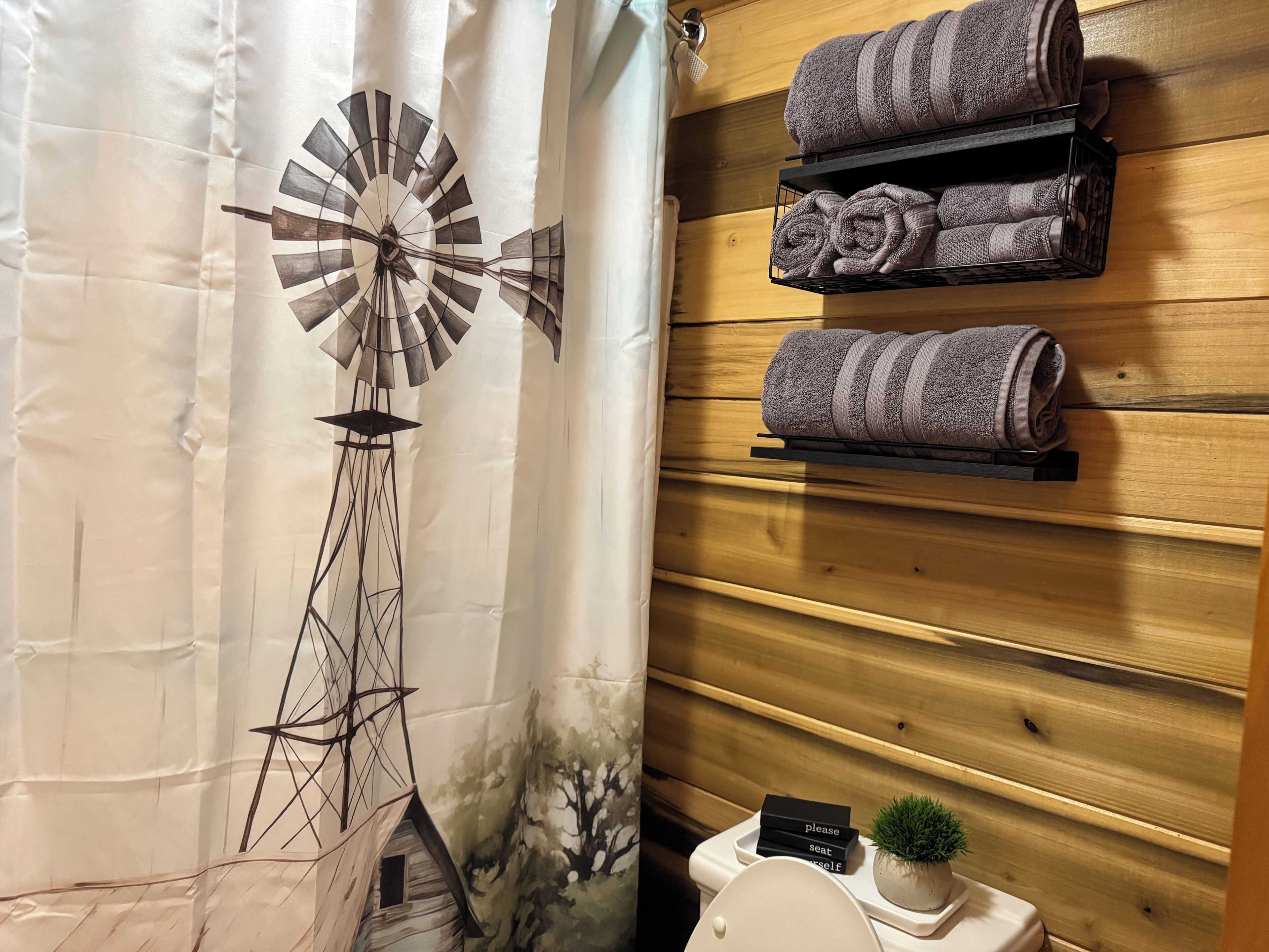 Une salle de bain décorée d’une fresque représentant un moulin à vent, avec des serviettes sur un porte-serviettes et une petite plante en pot.