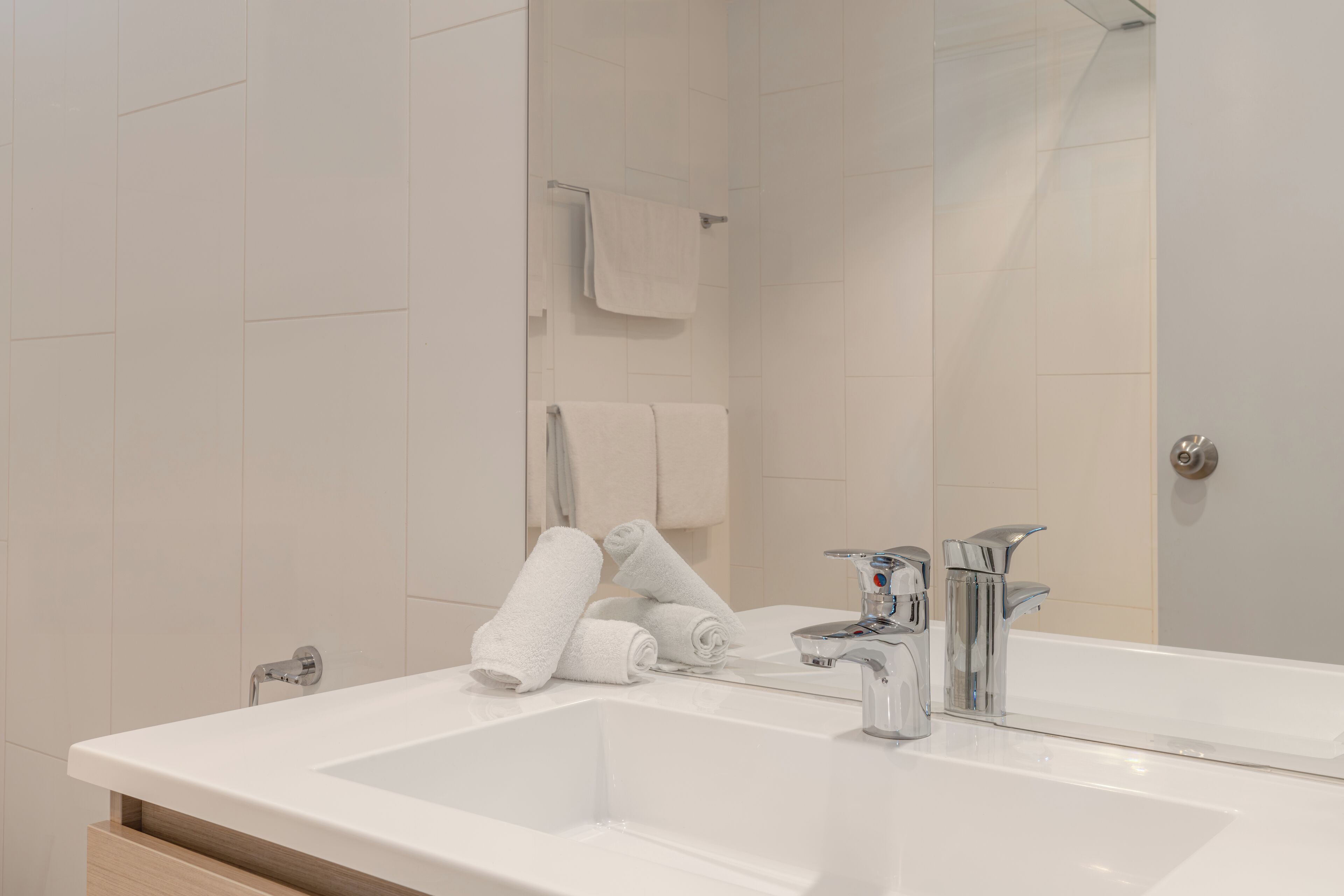 Un baño moderno con un lavabo blanco grande, dos sujetahilos con toallas blancas, y un espejo que refleja el ambiente.