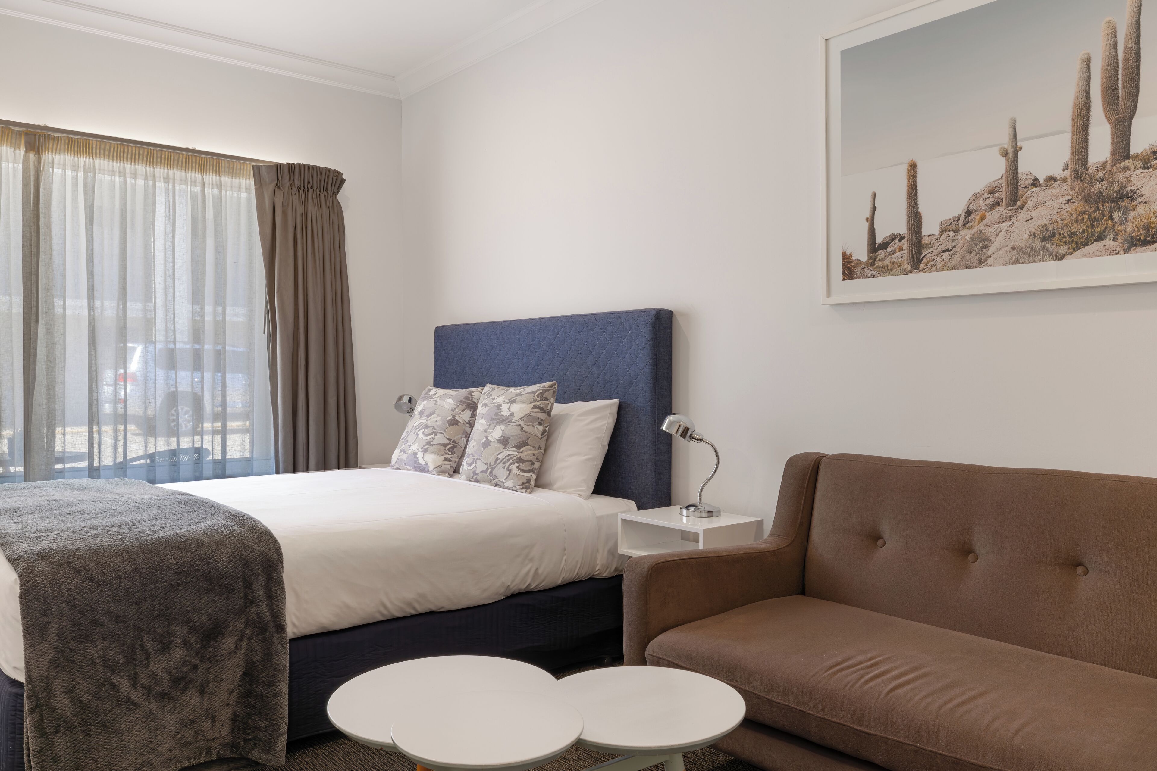 Una habitación de hotel con cama, sofá, dos mesitas, una mesita de noche y un cuadro en la pared.