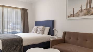 Una habitación de hotel con cama, sofá, dos mesitas, una mesita de noche y un cuadro en la pared.