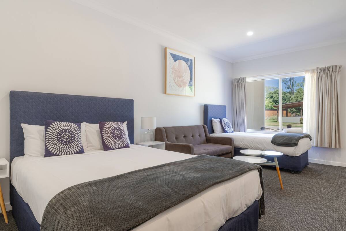 Una habitación de hotel con una cama grande, un sofá, una mesita y una ventana con cortinas.