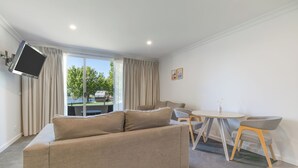 Un salon moderne comprenant un canapé, un téléviseur fixé au mur, un coin repas avec une table et des chaises, ainsi que de grandes fenêtres avec des rideaux.