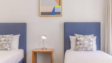 A hotel room with two beds, each with a headboard, a bedside table with a lamp, and a framed abstract painting on the wall.