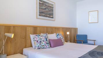 A neatly arranged hotel room with a bed, a chair, a desk, and a lamp.