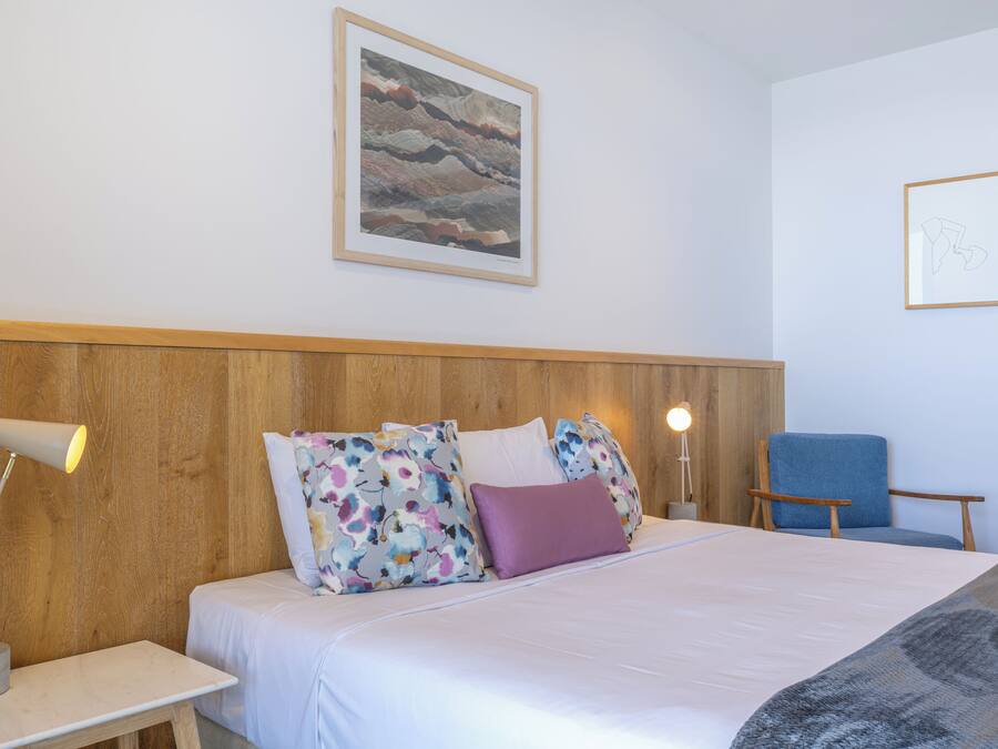 A neatly arranged hotel room with a bed, a chair, a desk, and a lamp.