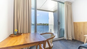 Une pièce avec une table en bois, une chaise, un vase avec une fleur et une vue sur l’extérieur, visible à travers une porte vitrée.