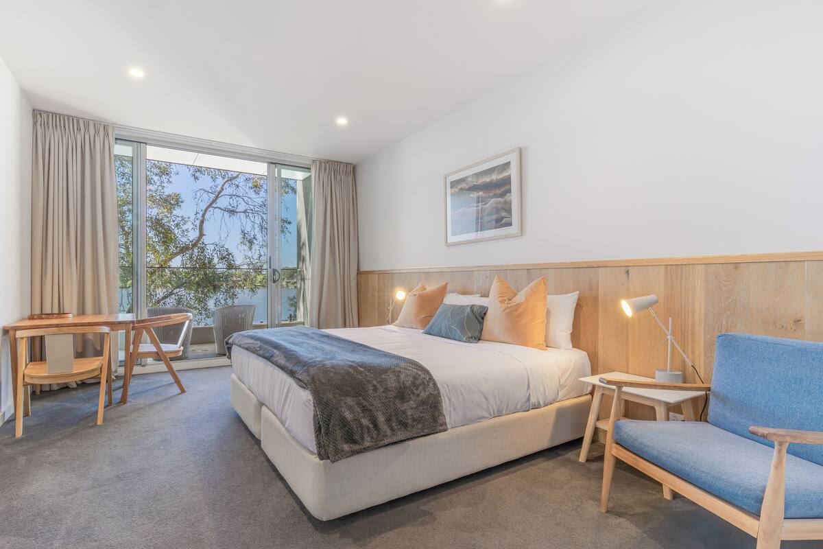 Una habitación de hotel moderna con una cama grande, un escritorio, una silla y vistas al exterior.